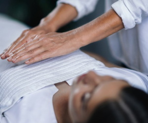 A reiki practiitoner holding their hands over a patient's torso. 
