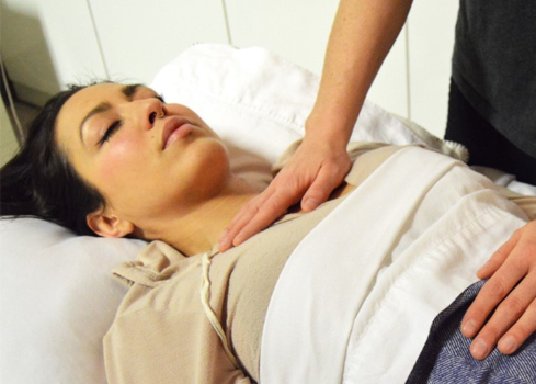 A reiki practitioner placing their hands on a client's clothed abdomen and upper torso. 