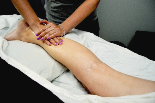 A massage therapist works on a client's strategically uncovered leg.